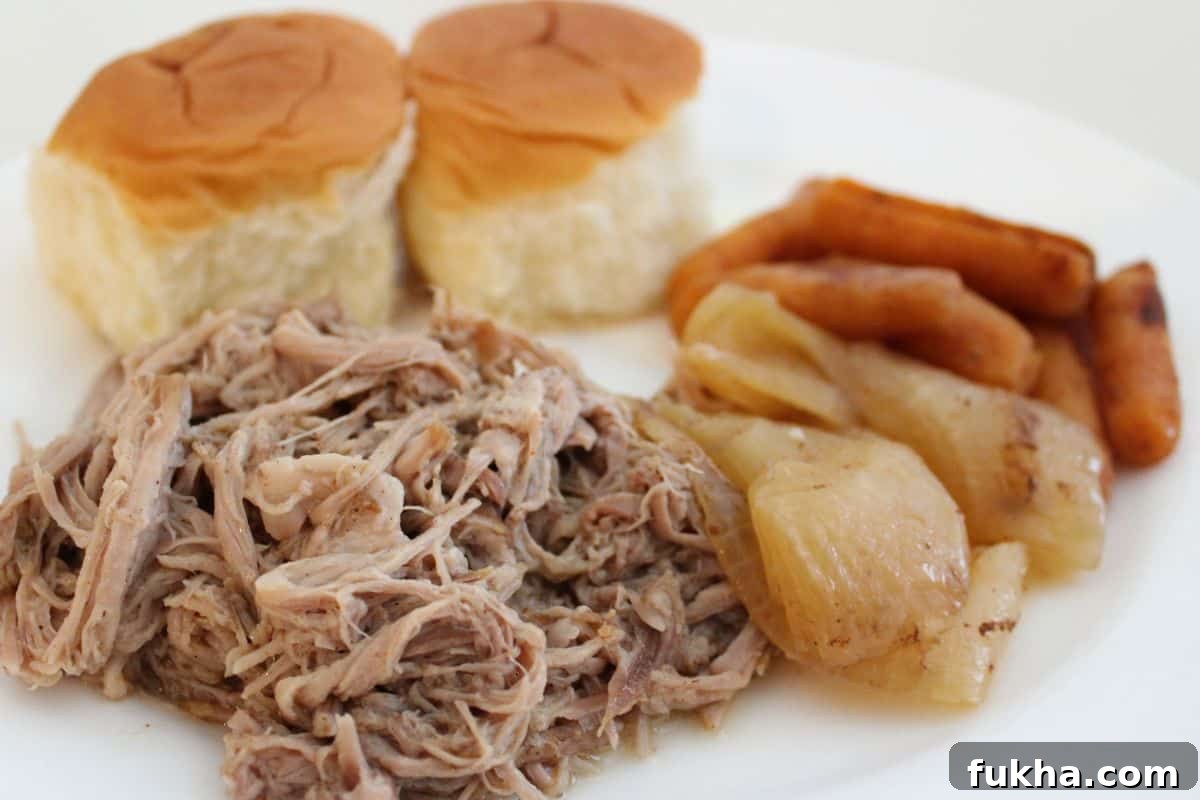 A plate with shredded pulled pork, two bread rolls, roasted onions, and cooked carrots.