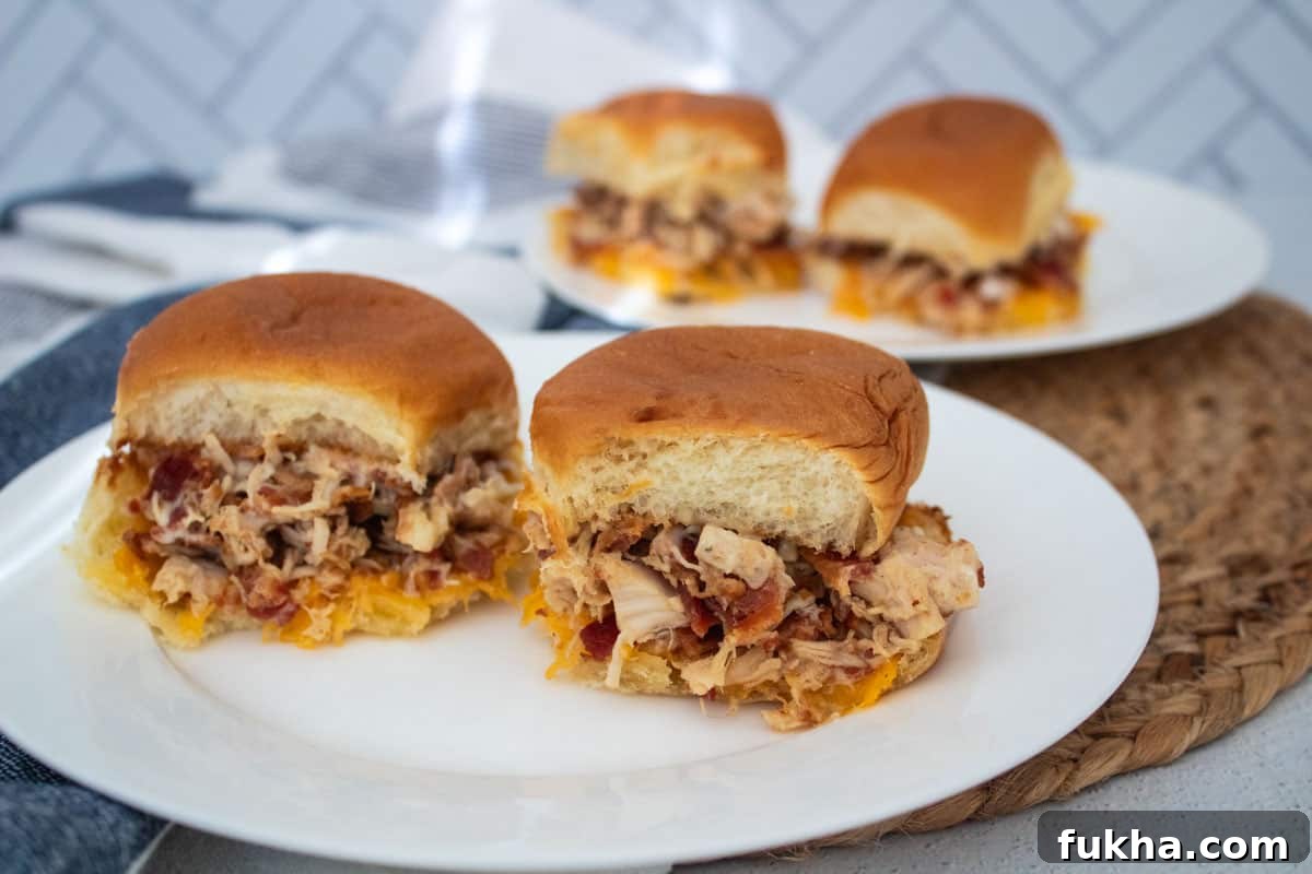Four sliders stuffed with a bacon chicken mix, cheddar cheese, and ranch dressing, split between two white plates.