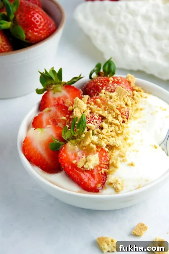Smooth cottage cheese in a white bowl topped with strawberries and graham cracker crumbs, placed on a white marble counter.