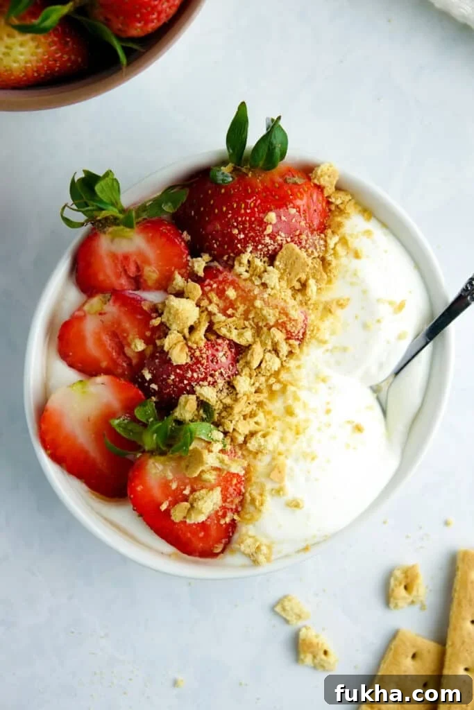 Smooth cottage cheese in a white bowl with strawberries and graham cracker crumbs, placed on a white marble counter.