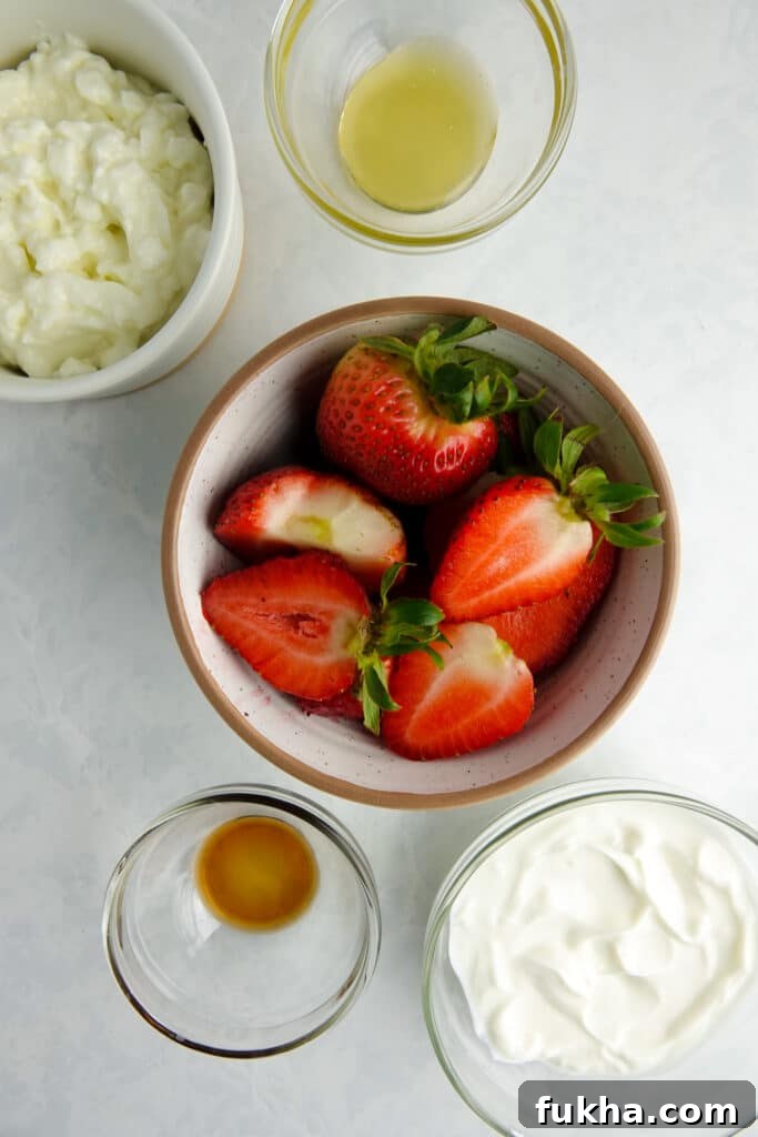 Ingredients for a healthy blended cheesecake bowl in bowls on a white counter - including honey, cottage cheese, greek yogurt, vanilla extract and strawberries.