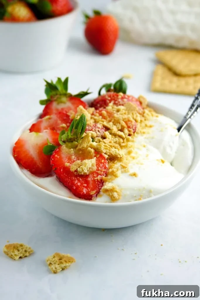 Smooth cottage cheese in a white bowl with strawberries and graham cracker crumbs, placed on a white marble counter.