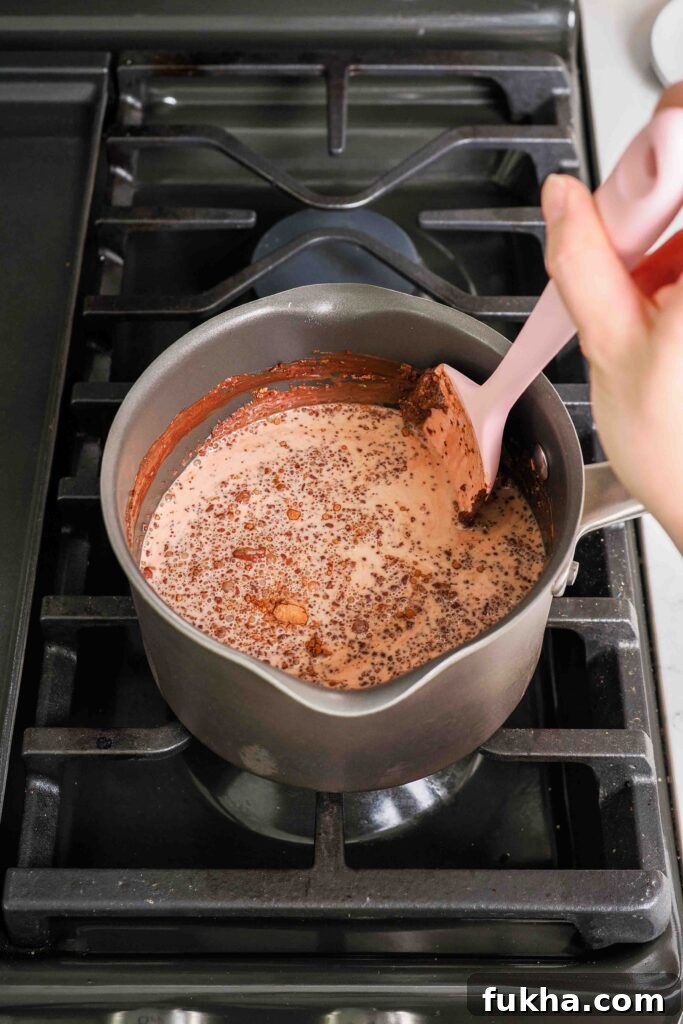 A spatula presses cocoa powder into the side of a pot filled with milk and cream to help it dissolve.