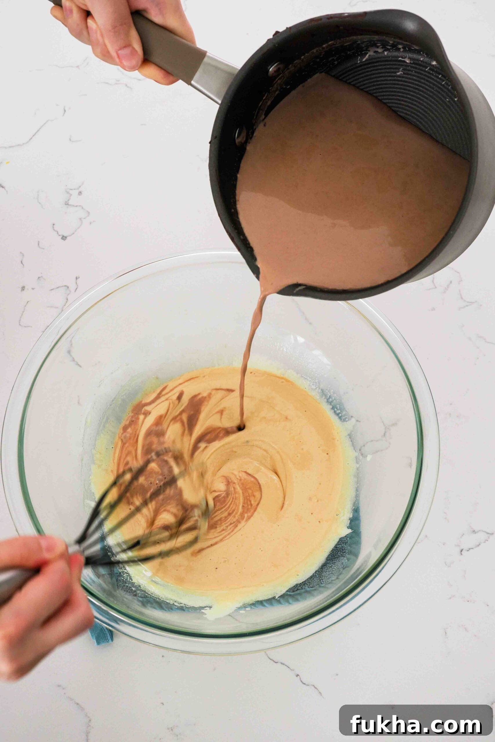 Warmed chocolate cream is poured into ribboned egg yolks to temper them.