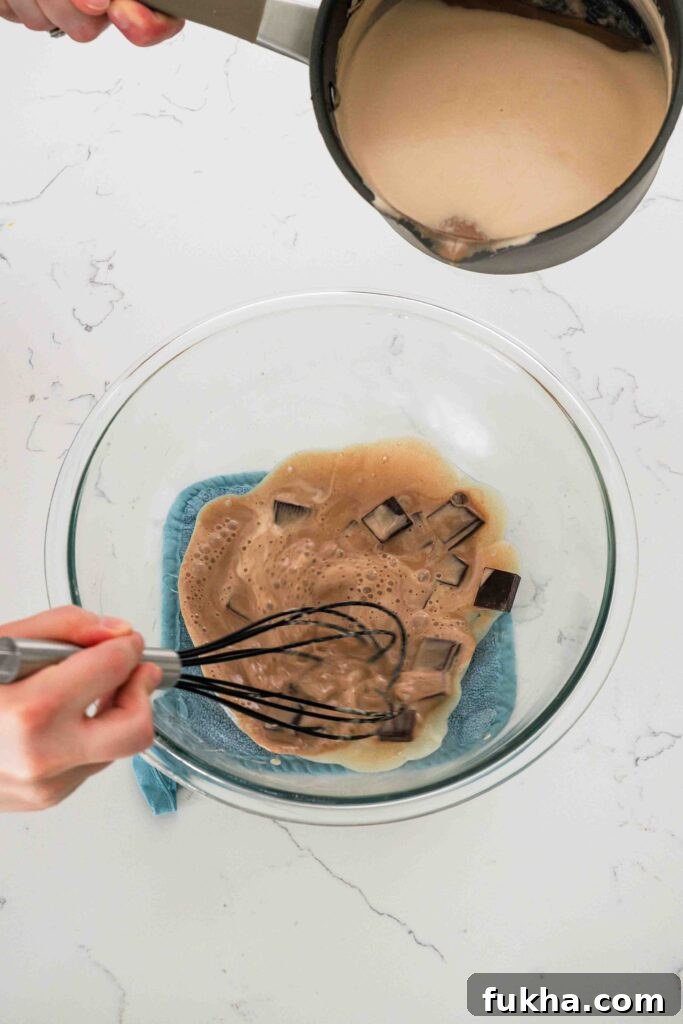Warmed cream is poured onto chocolate in a large mixing bowl to melt it.