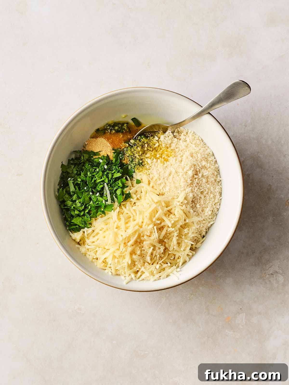 Dump-and-Bake Chicken Kyiv with Creamy Orzo 7 A bowl with breadcrumbs, cheese, oil and parsley in, with a spoon ready to stir.