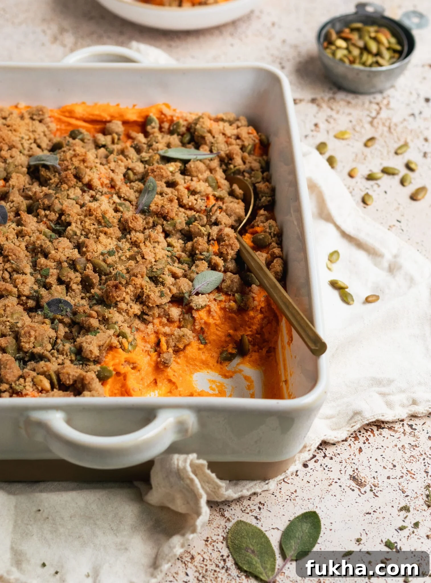 sweet potatoes in a white casserole dish topped with a brown sugar pepitas topping and fresh sage. 