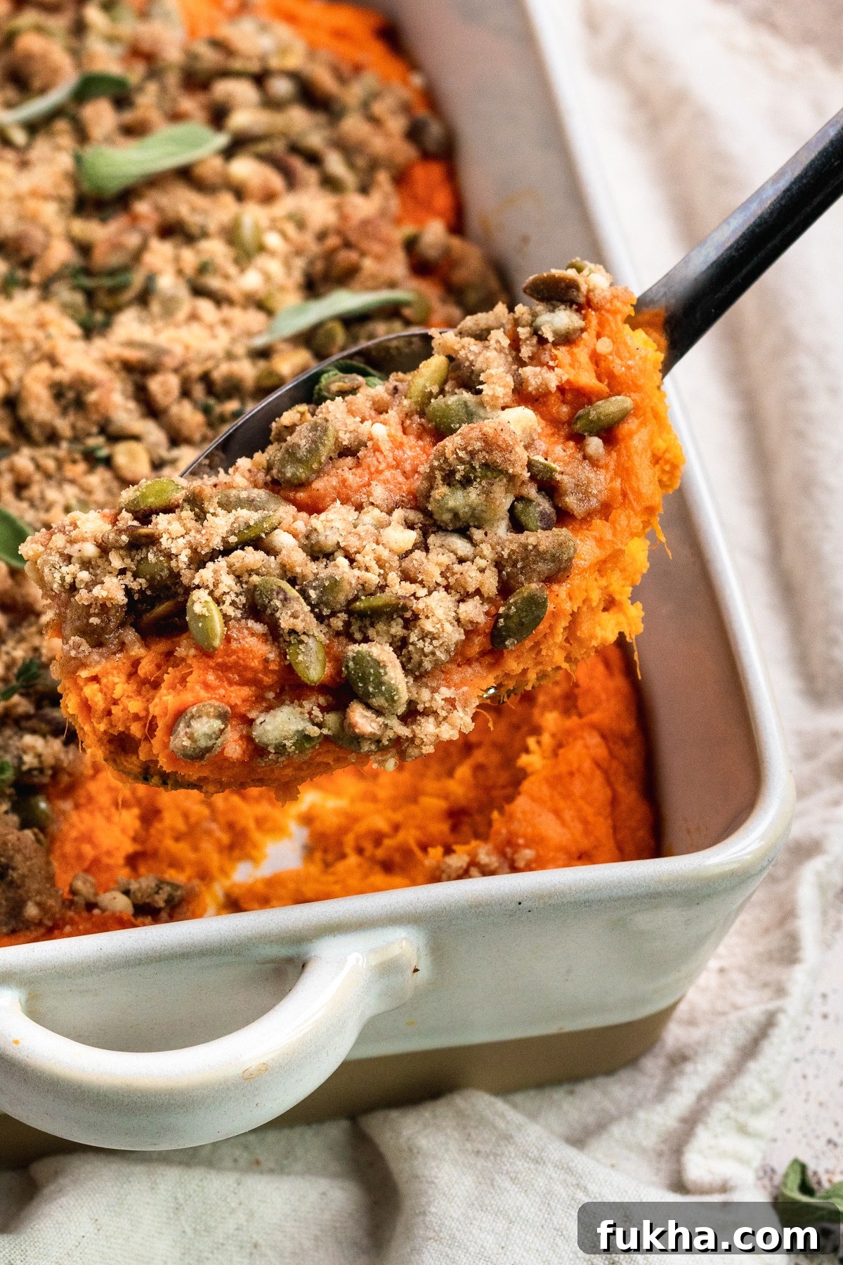 am up close image of a black spoon scooping out sweet potato casserole from a white casserole dish.