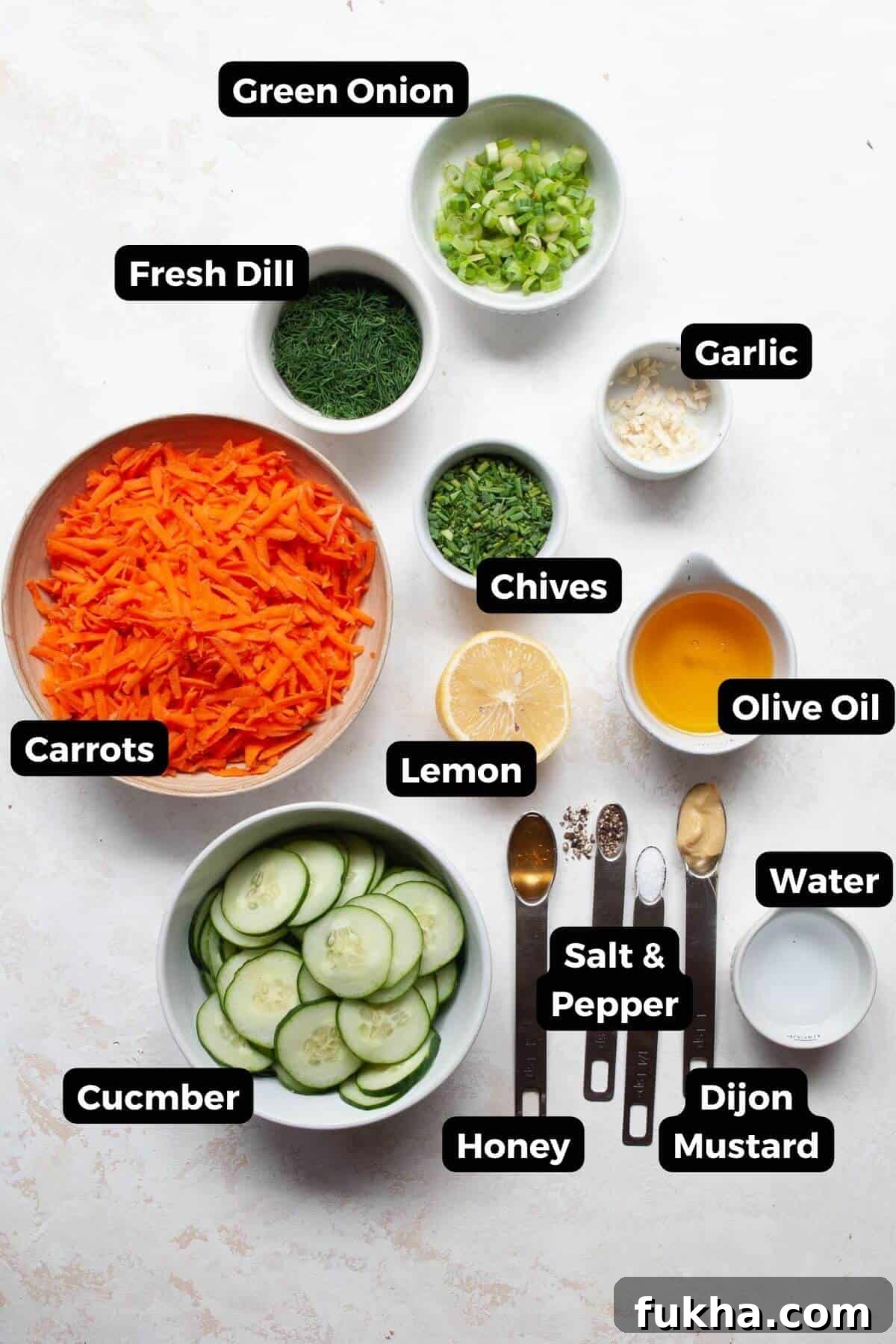 All ingredients in small bowls with labels including cucumber, carrots, olive oil, dijon mustard, garlic, salt, pepper, fresh herbs, green onion, and honey.