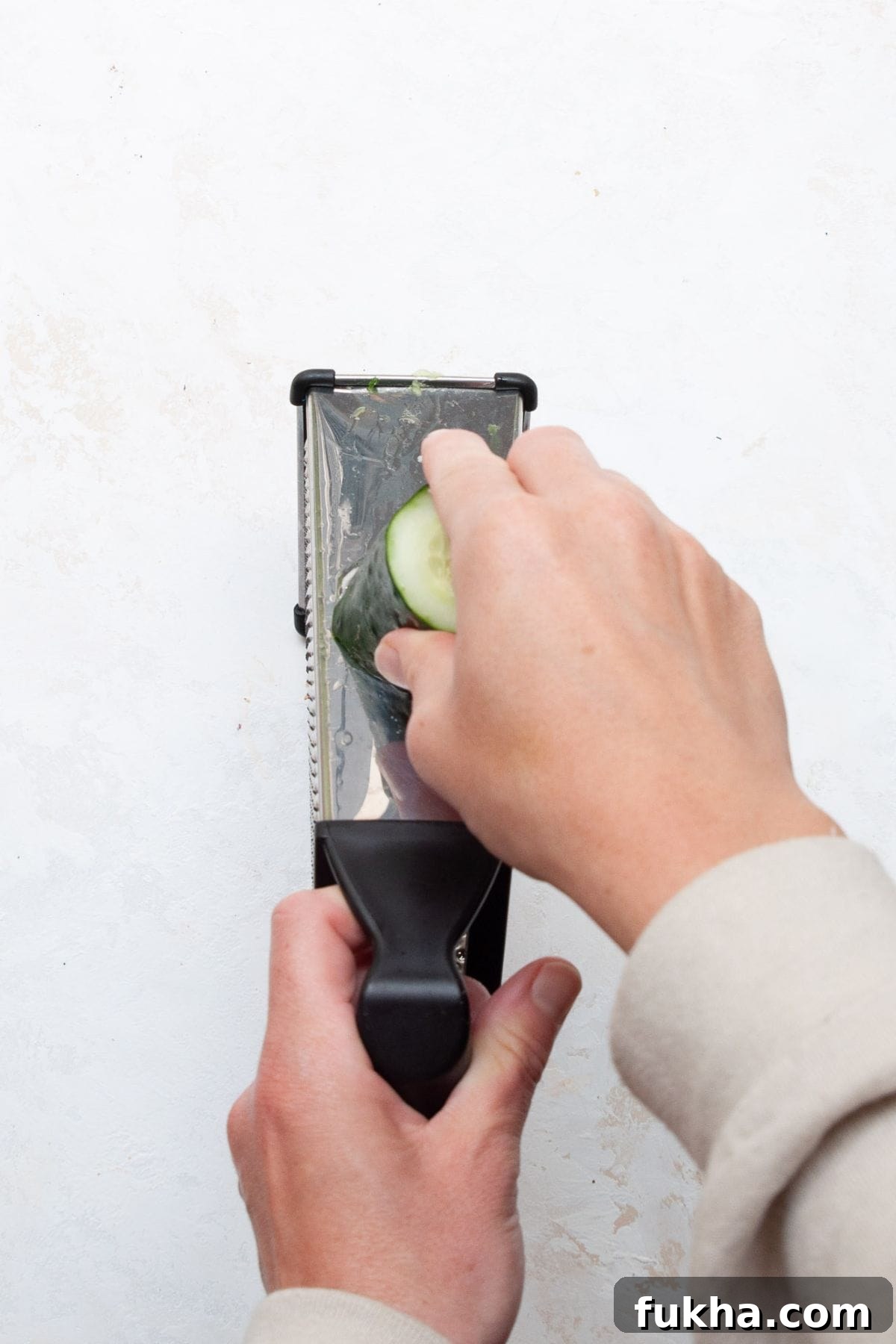 Thinly slicing a cucumber on a box grater.