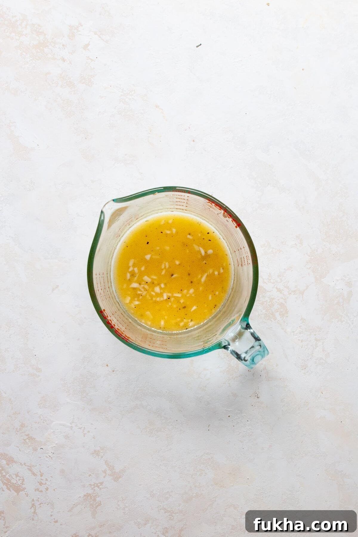 Whisking homemade healthy apple cider vinaigrette in a measuring cup.