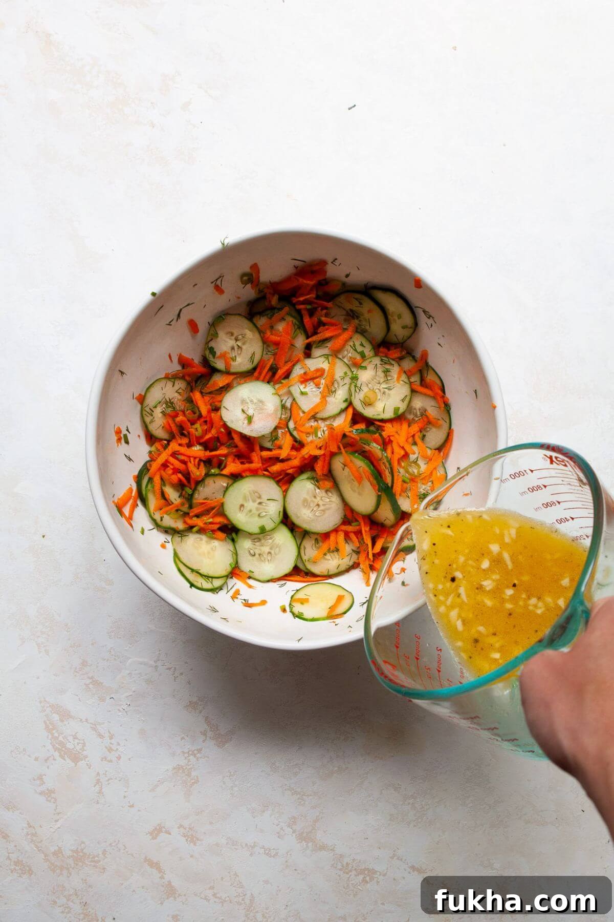 Pouring easy apple cider vinaigrette on top of salad in mixing bowl.