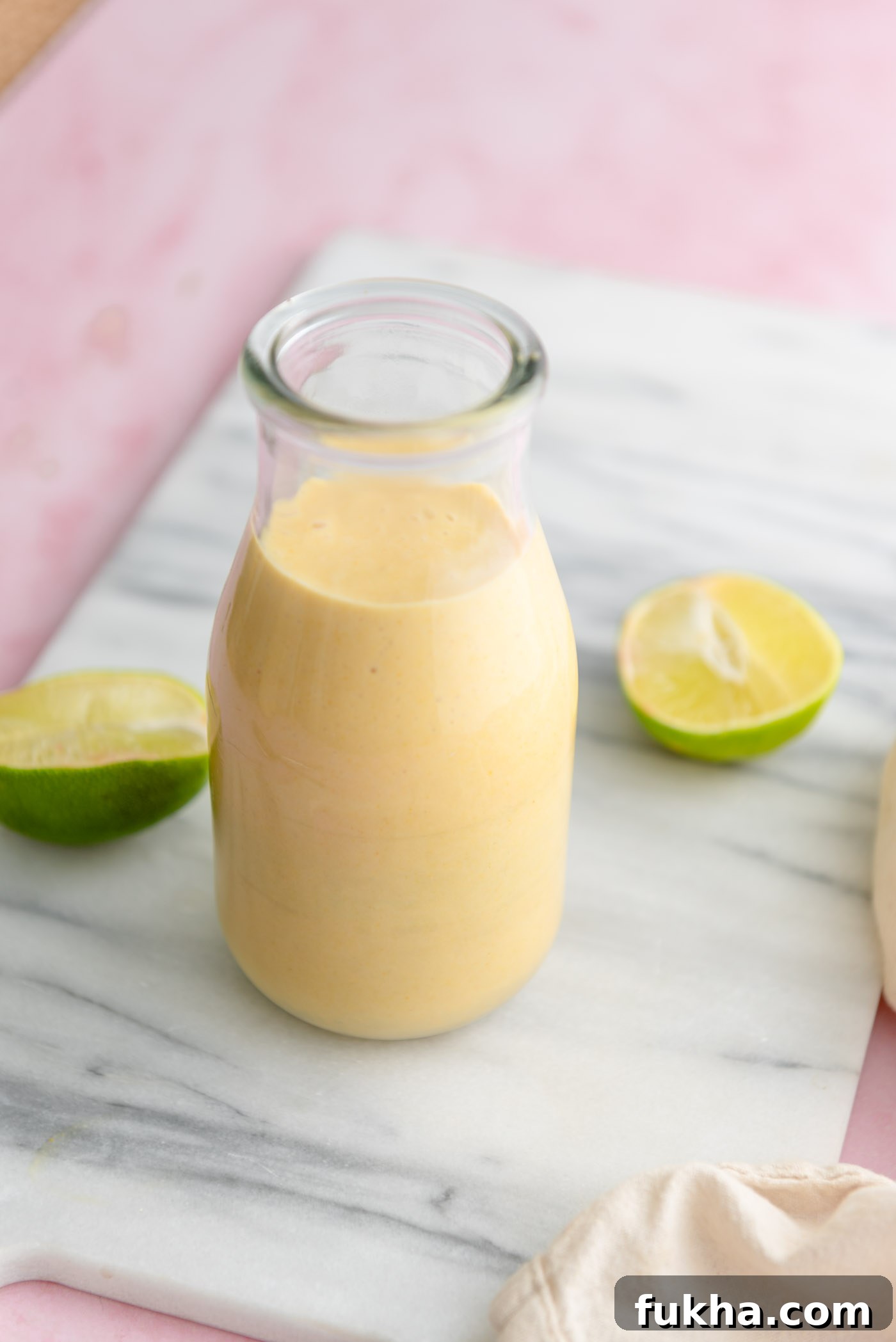 Creamy mango coconut smoothie in a glass milk jar on a marble cutting board with two lime halves beside the glass.