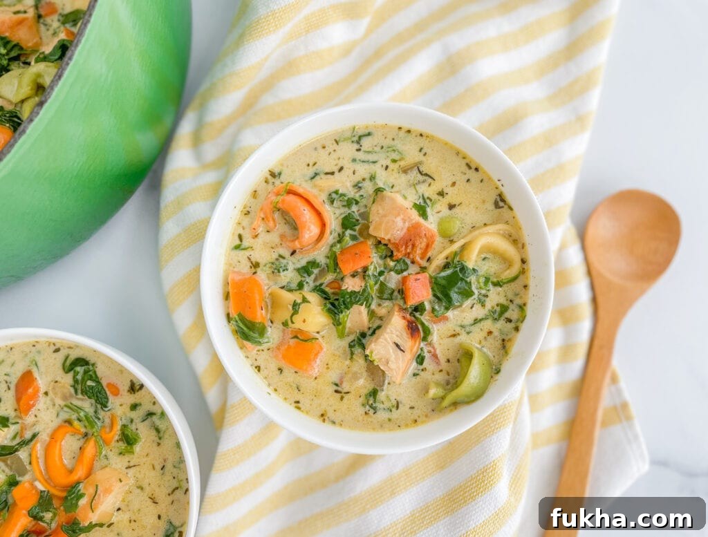 A bowl of soup with tortellini, cream broth, carrots and spinach showing. The bowl is sitting on a yellow striped napkin.