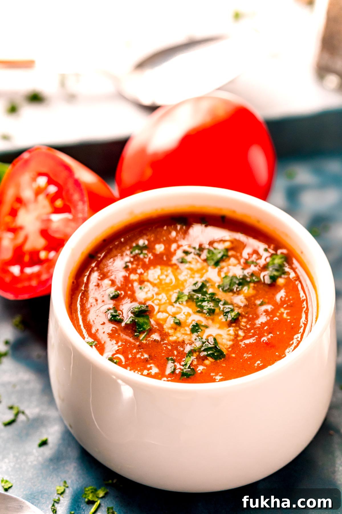 Close up photo of tomato soup in a white bowl topped with parmesan cheese and parsley.