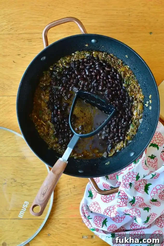 A pot of black beans with a potato masher in it. 