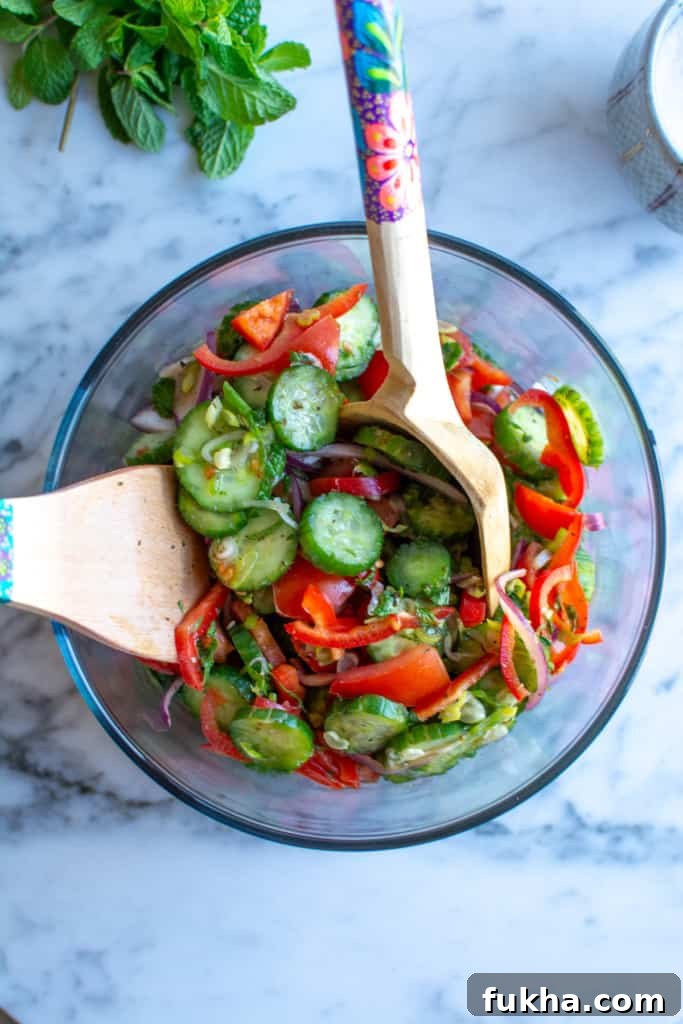 A glass bowl with Mexican cucumber recipe and two salad scoopers.