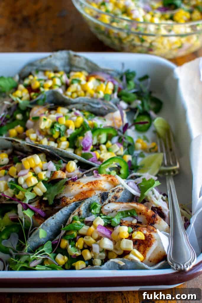 Several grilled fish tacos in a white tray topped with corn ssalsa.