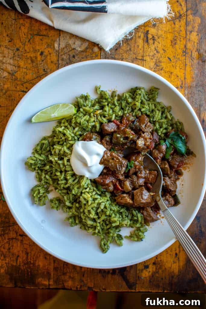 A white bowl on a wood table filled with carne picada, green rice and topped with sour cream.