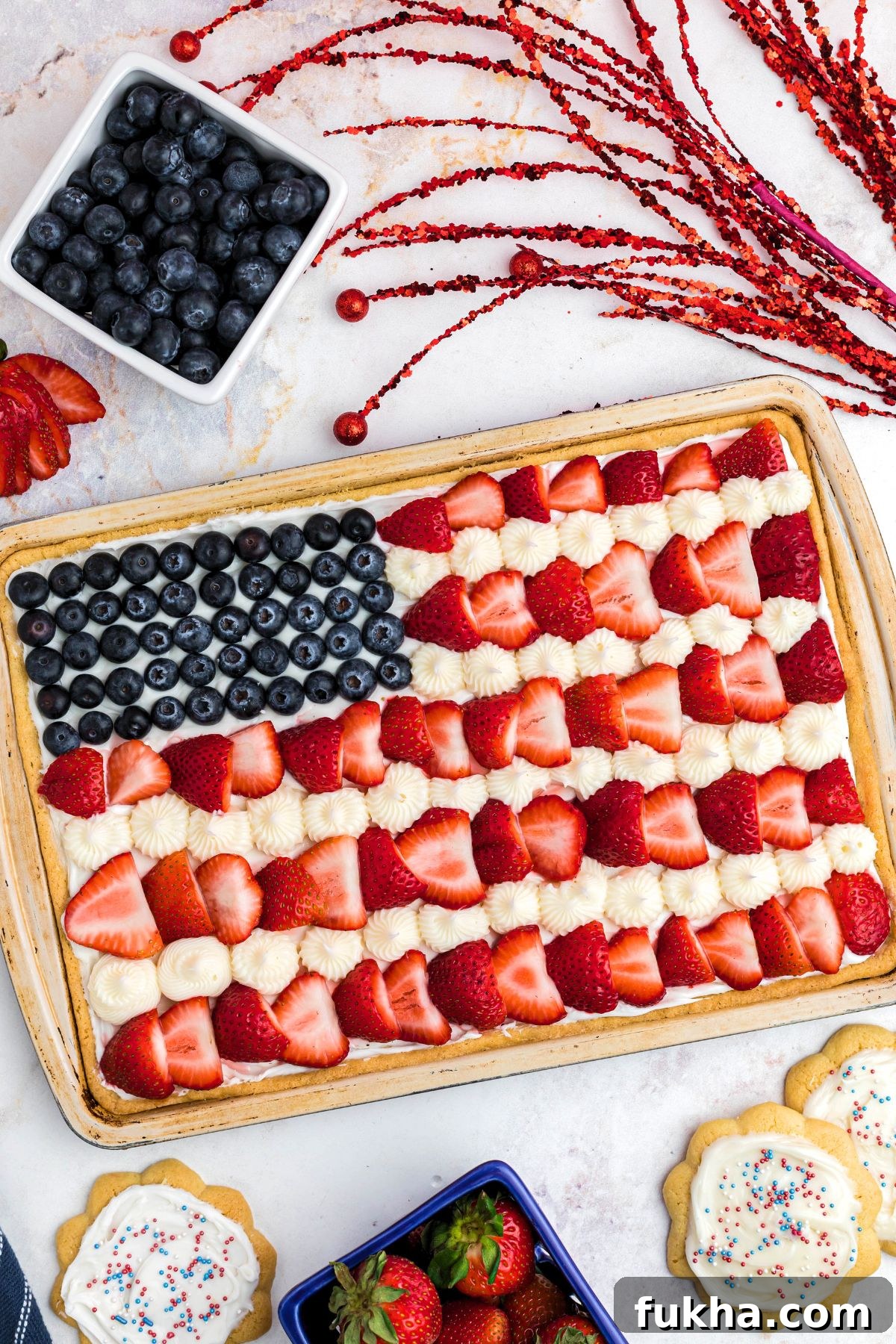 Fourth of July American Flag Fruit Pizza Recipe 2 Rectangle cookie in cookie pan, topped with frosting, blueberries and strawberries, on a marble table.