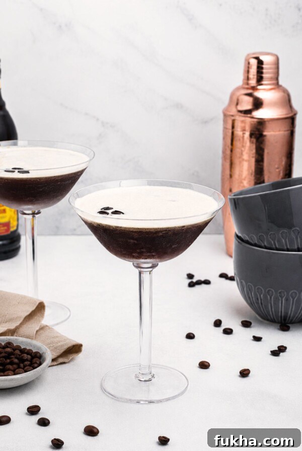 Martini glass with coffee and vodka mixture, with a frothy foam on top, on a marble table with coffee beans scattered.