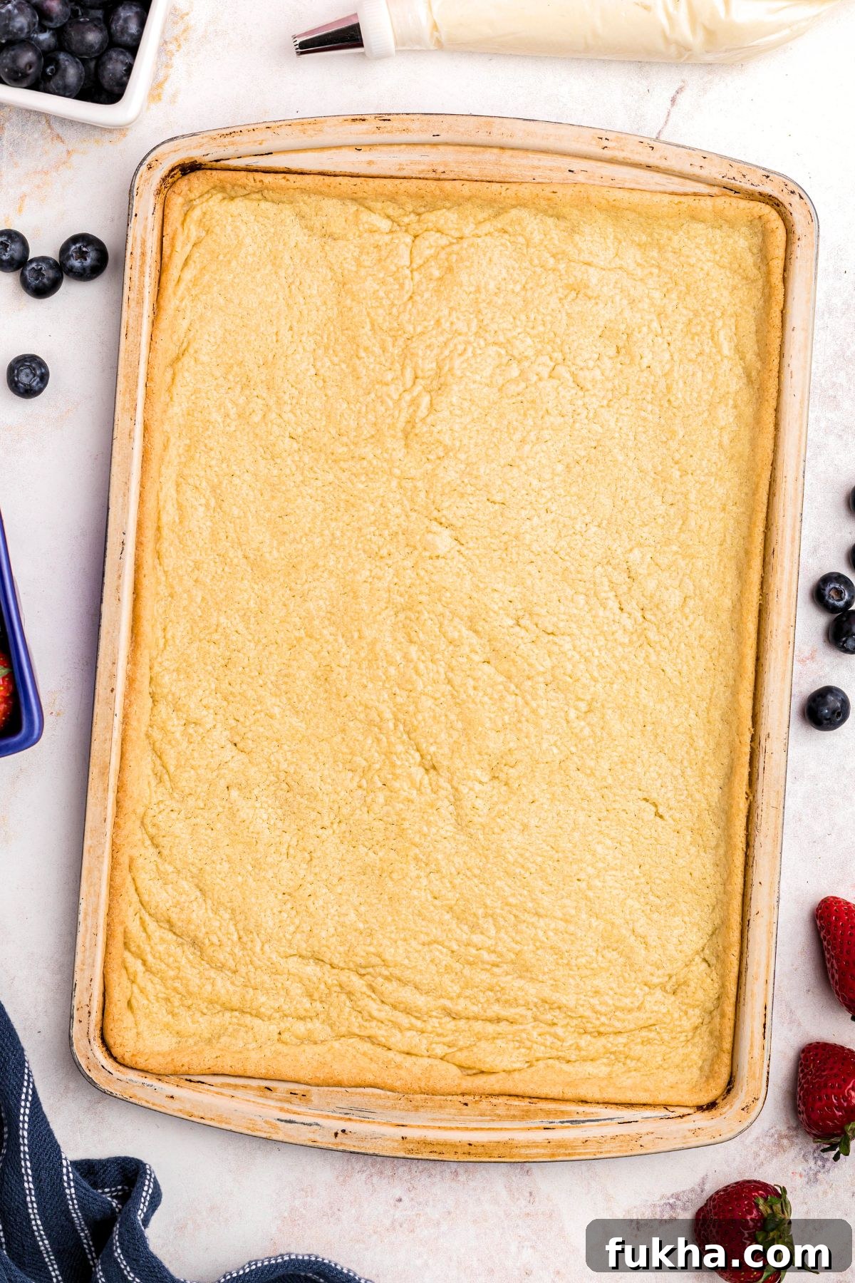 Fourth of July American Flag Fruit Pizza Recipe 4 Sugar cookie baked into baking sheet with fresh fruit scattered around the table.