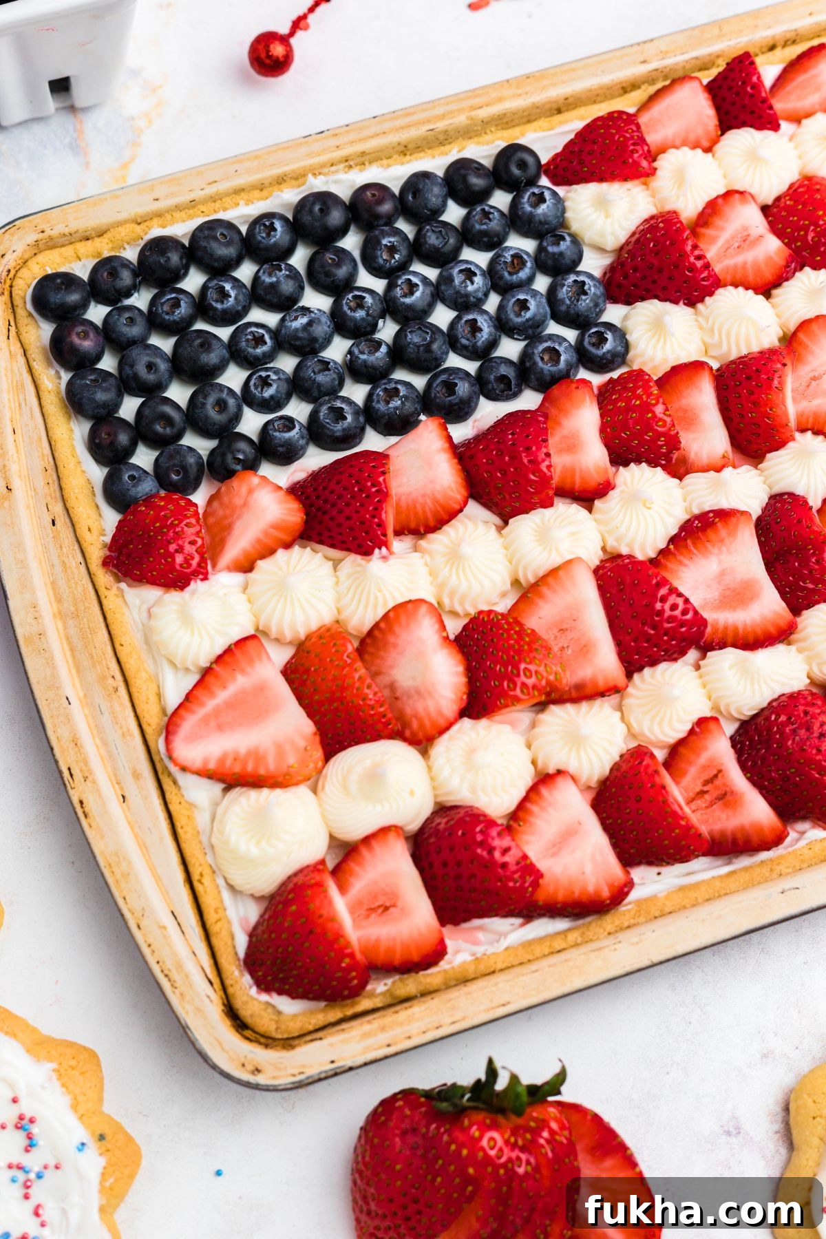 Fourth of July American Flag Fruit Pizza Recipe 8 Fruit and frosting, decorating cookie, with berries on the table.