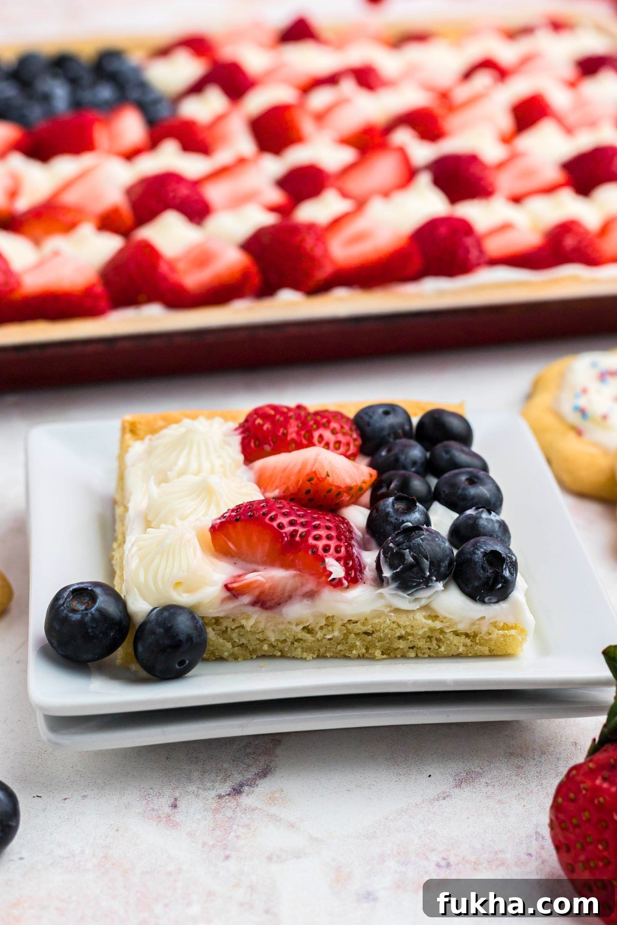 Fourth of July American Flag Fruit Pizza Recipe 10 slice of American flag fruit pizza cut and served on a small white square. plate.