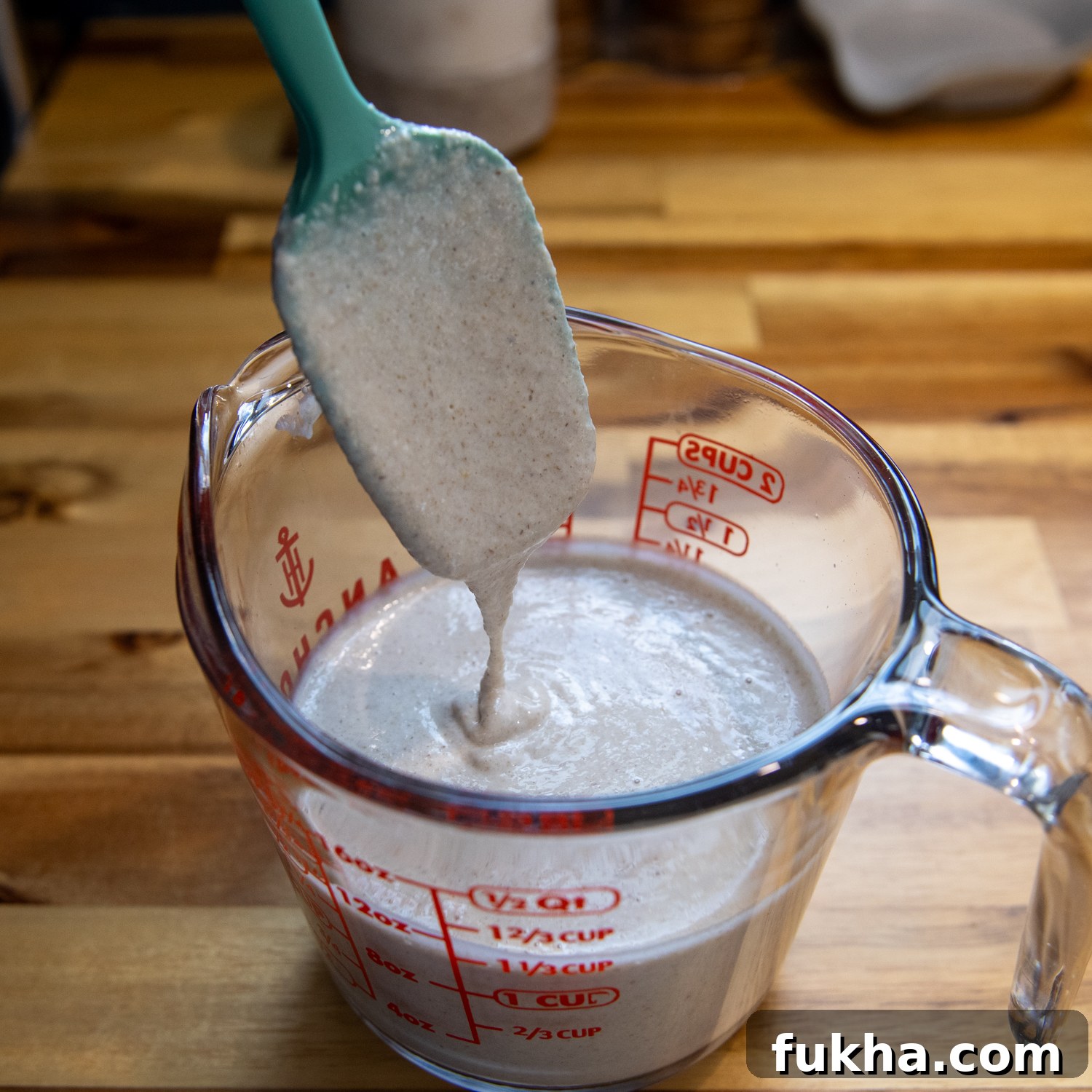 Tortilla ingredients mixed and in a glass measuring cup with a spatula showing consistency.