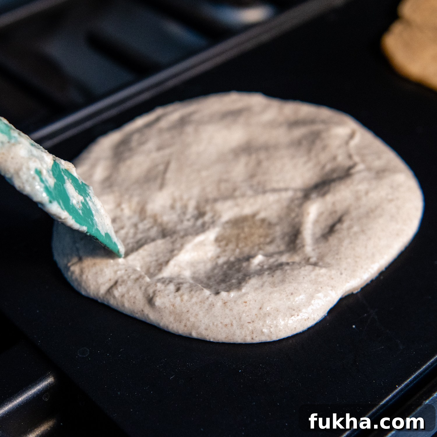 Spatula spreading tortilla mix on griddle.