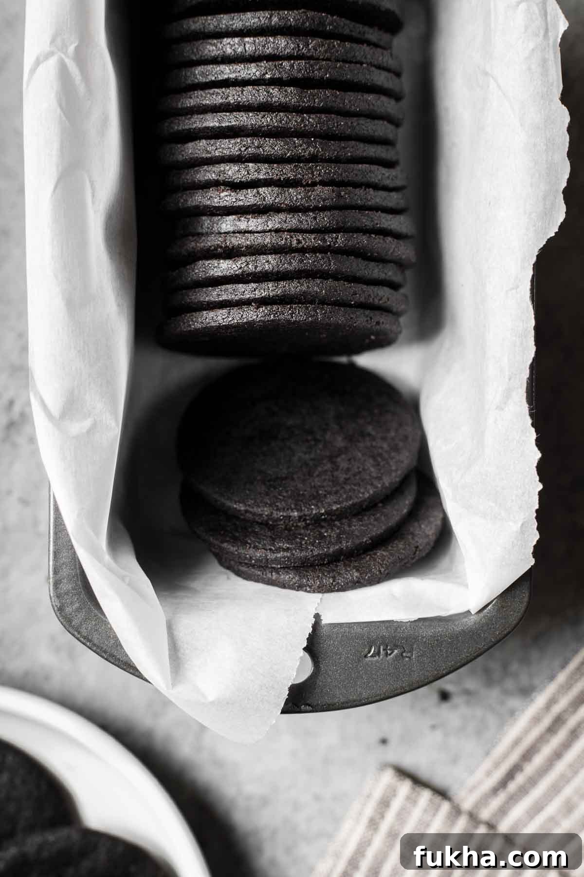 Crispy Homemade Chocolate Wafer Cookies Recipe 14 Round black cookies in a parchment lined metal pan with a few tipped over.