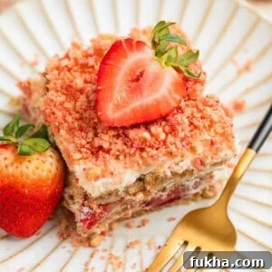 Layered strawberry icebox cake topped with strawberry crunch on plate with fresh strawberry garnish.