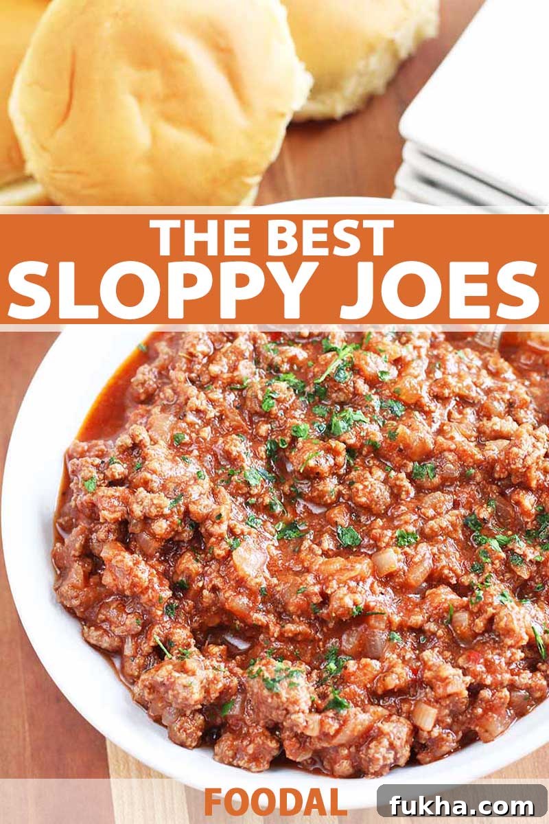 Upgraded Classic Beef Sloppy Joes Recipe 2 Top-down shot of a large white bowl filled with ground beef sloppy joe filling, topped with chopped parsley, with hamburger buns and a stack of square white plates on a brown wood table.