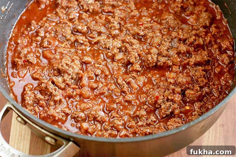 Upgraded Classic Beef Sloppy Joes Recipe 10 A large frying pan of ground beef in a red sauce, on a brown wood table.