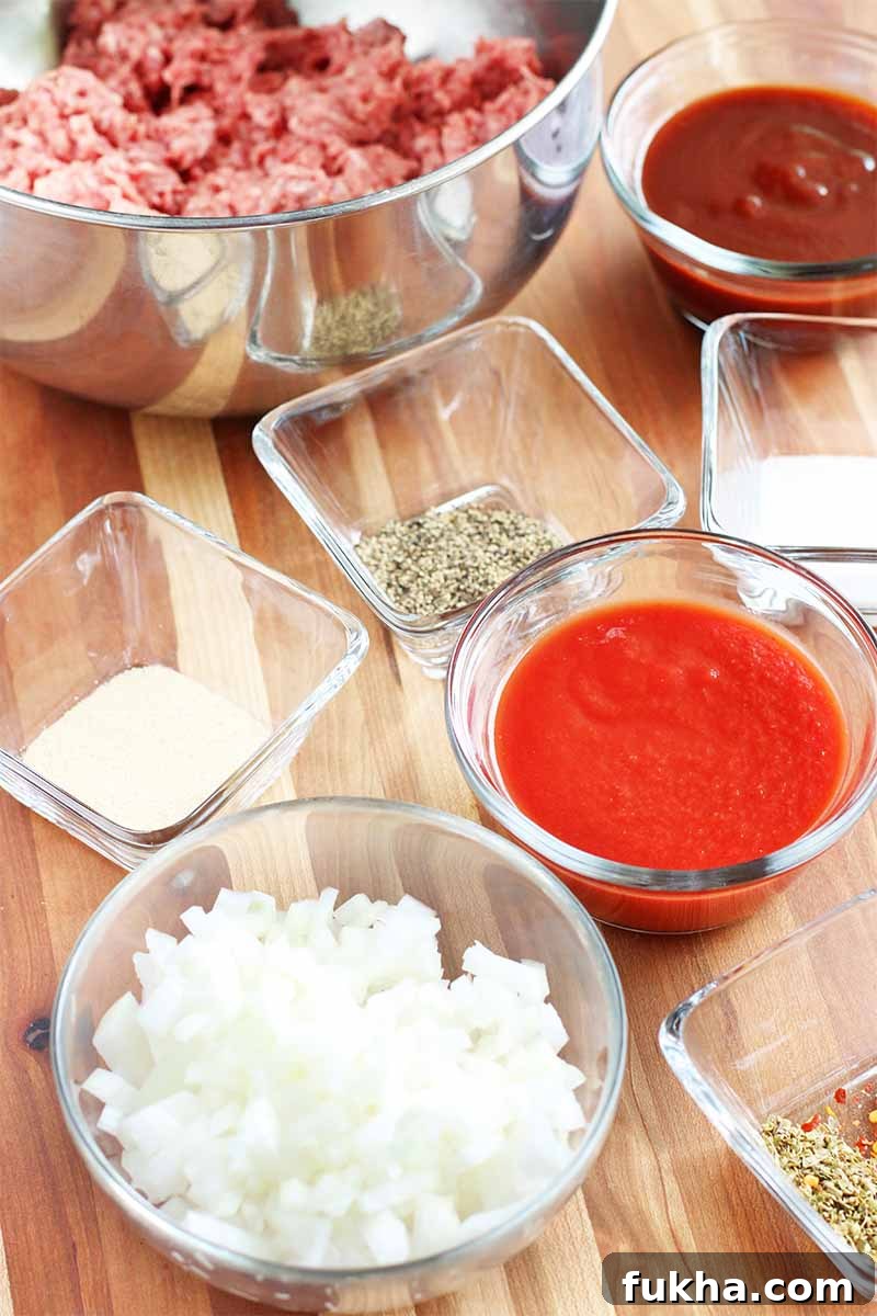 Upgraded Classic Beef Sloppy Joes Recipe 7 Small round and square bowls of red sauce, chopped white onions, spices, and a larger stainless steel bowl of raw ground beef, on a brown wood tabletop.
