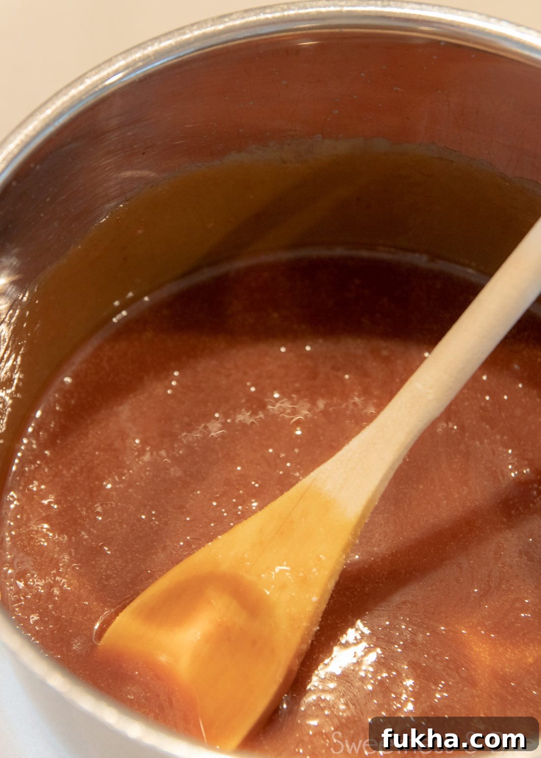 Decadent Caramel Mud Cake Recipe with Gluten Free Option 5 A saucepan with caramel sauce in it, with a wooden spoon.