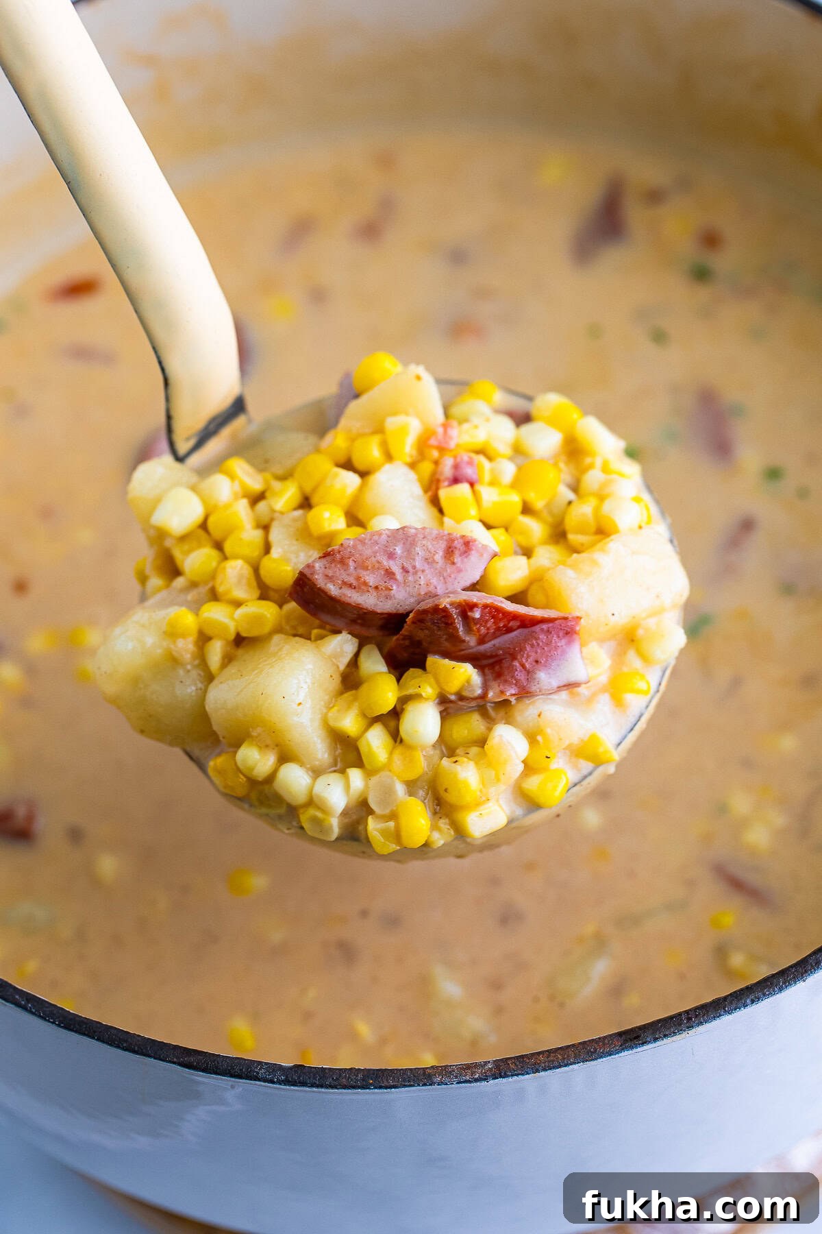 a serving spoon holding up a portion of Corn Chowder recipe over the Dutch oven