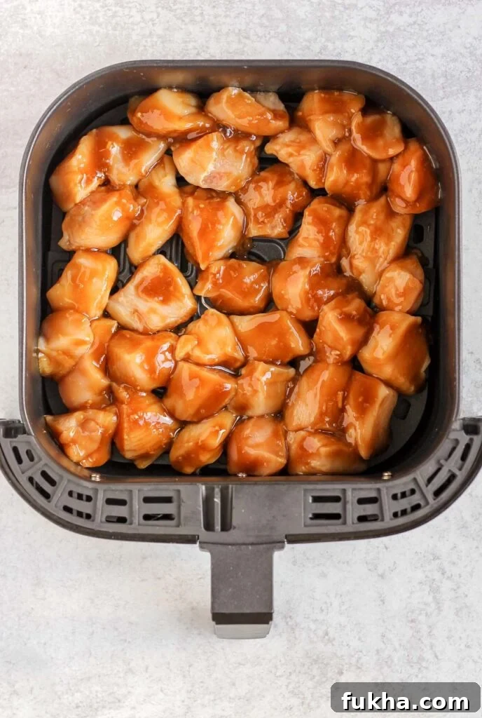 Raw chicken coated with teriyaki sauce in air fryer basket.