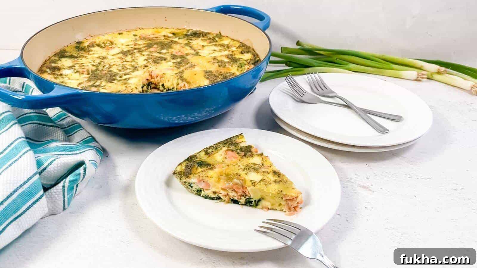 24 Low-Carb Breakfasts to Keep You Full Until Noon 22 A slice of vegetable and cheese frittata is served on a white plate beside a blue baking dish, with stacked plates, forks, green onions, and a striped towel nearby.