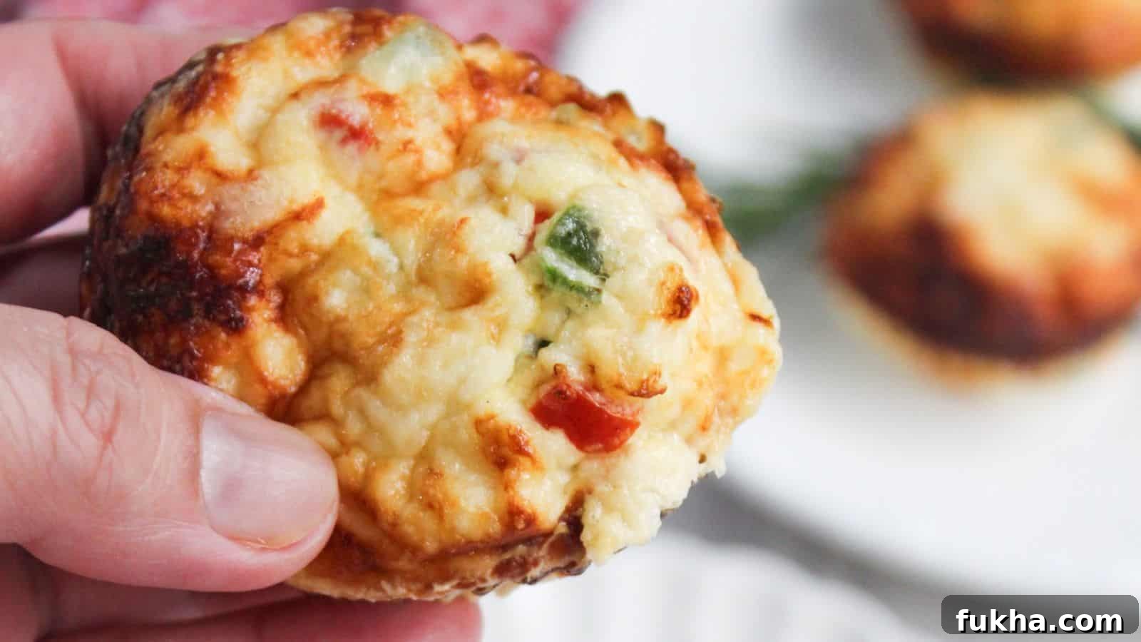 24 Low-Carb Breakfasts to Keep You Full Until Noon 5 A close-up of a hand holding an egg white frittata muffin with visible toppings of cheese and chopped peppers.