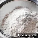 cake and pastry flour in mesh sifter set on top of parchment paper