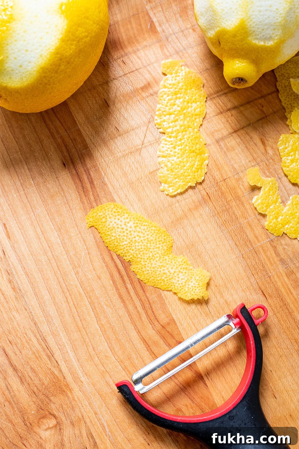 A thinly sliced lemon peel from a y- peeler with minimal white pith on a wooden cutting board.