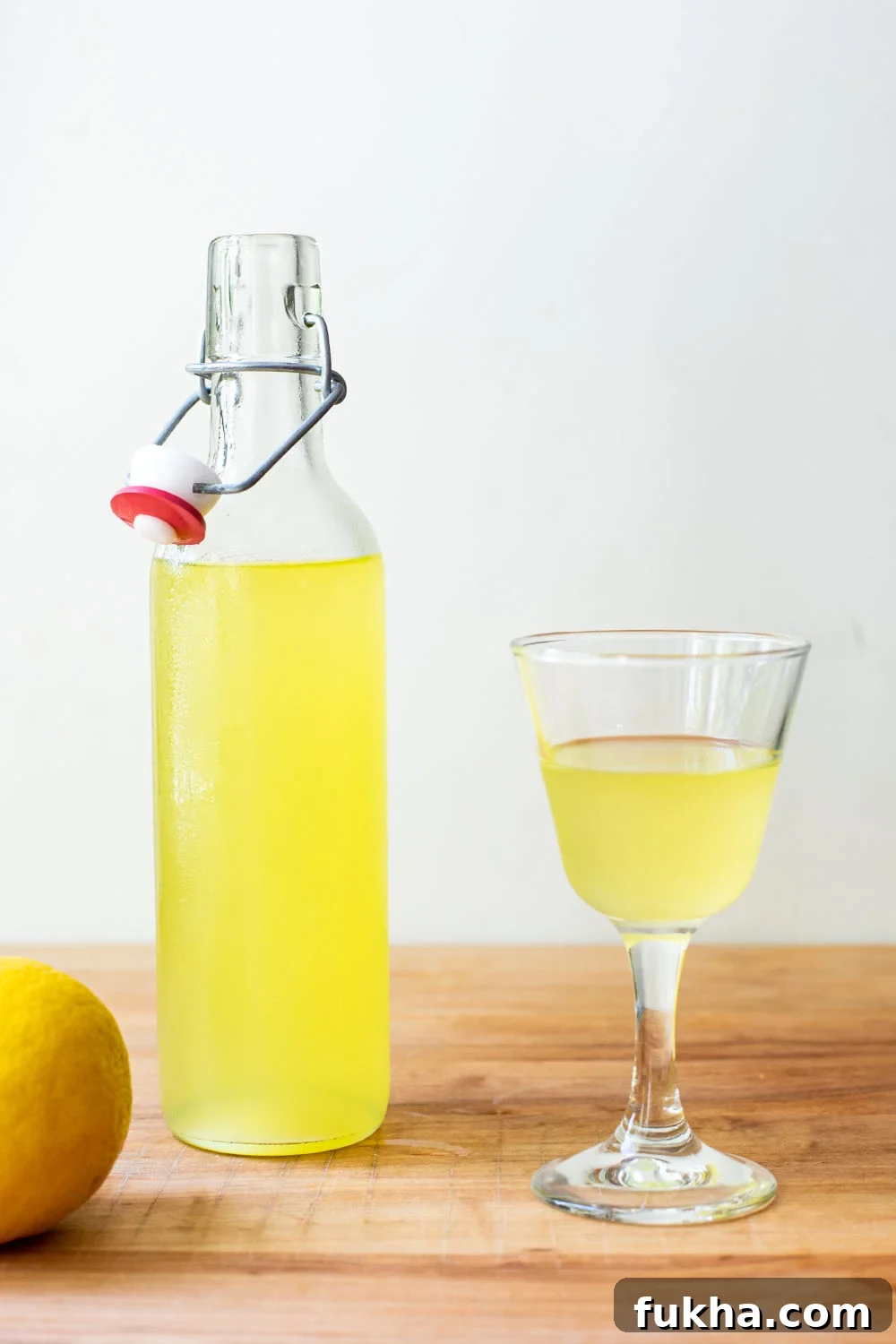 A bottle of finished limoncello next to a small glass serving of limoncello.