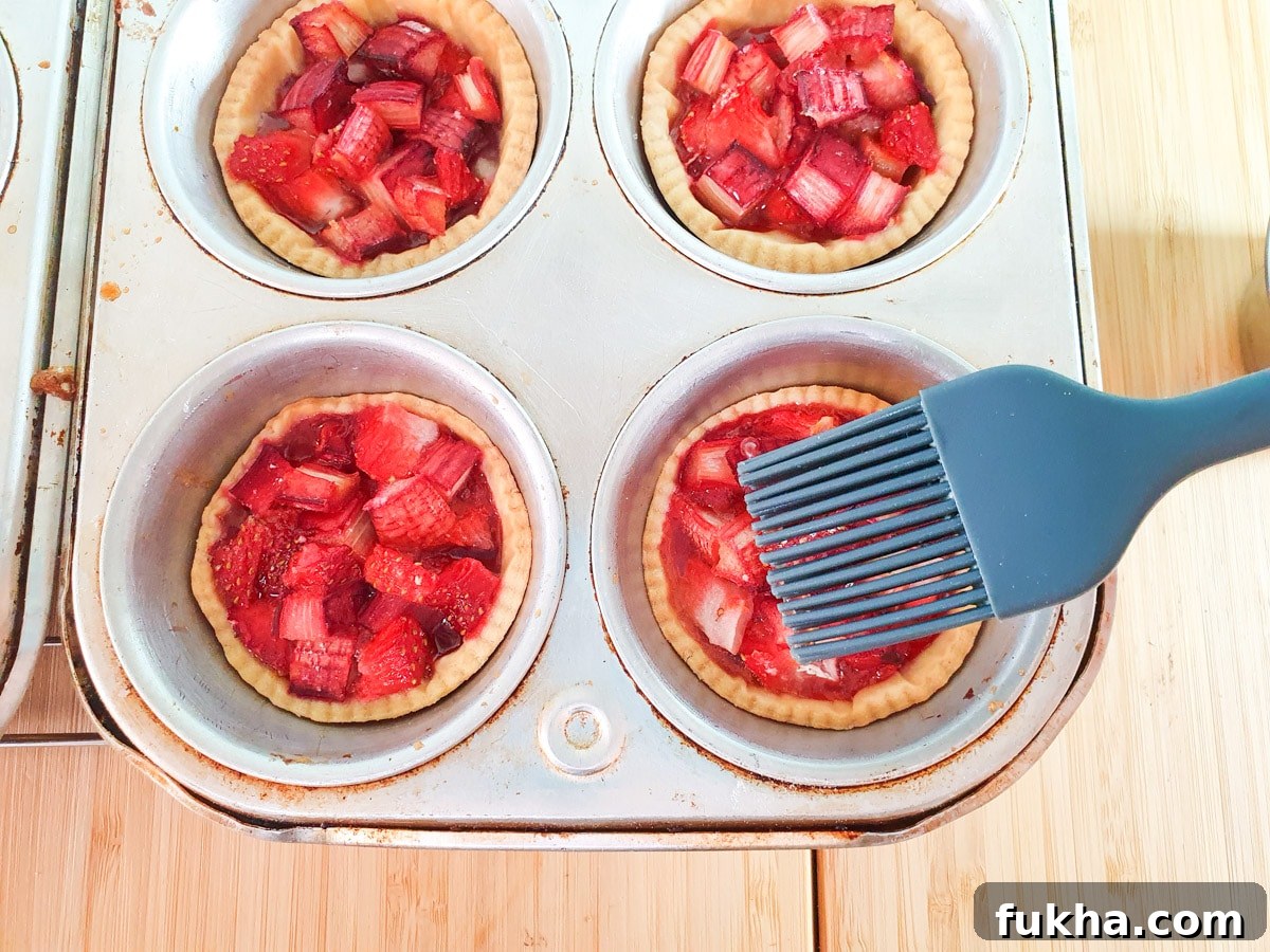 Brushing strawberry jam onto just baked tartlets.