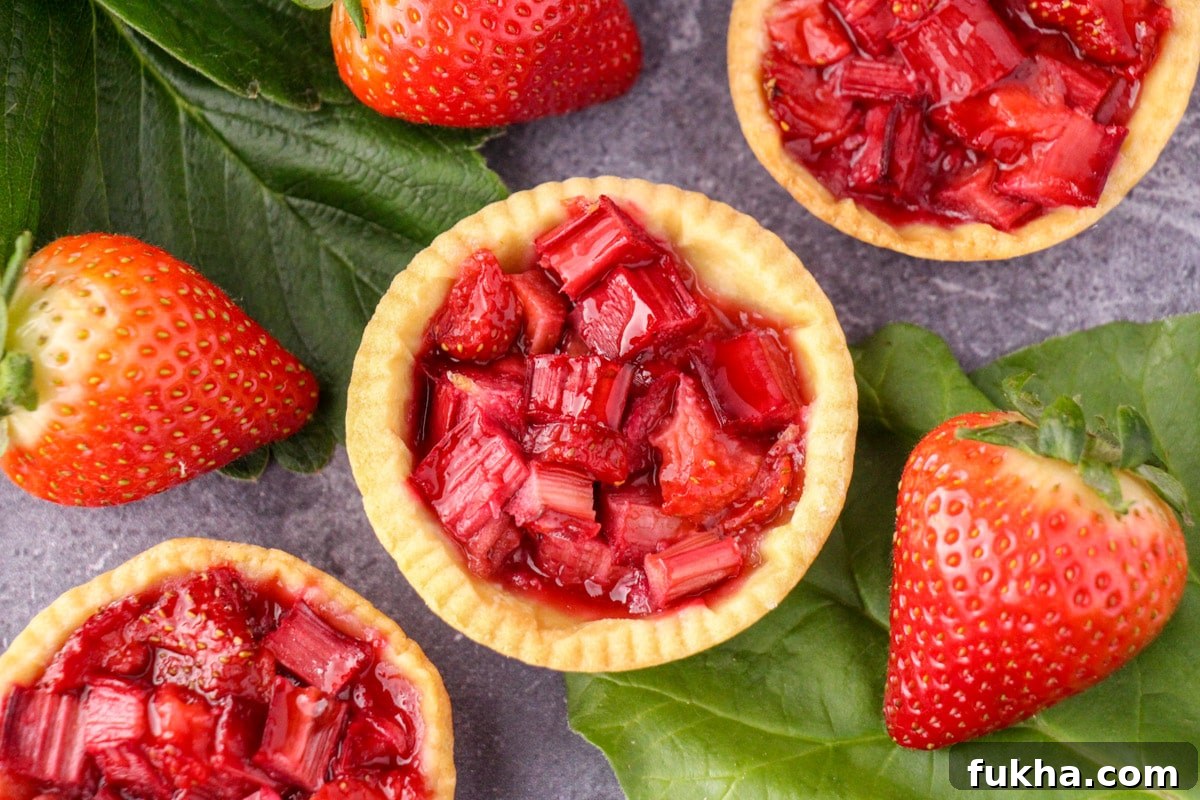 Close up strawberry rhubarb tartlets with strawberry and rhubarb leaves and fresh strawberries.
