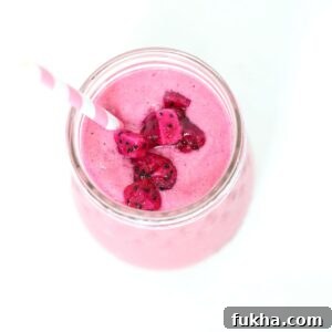 Top view of a pitaya smoothie in a glass jar topped with pieces of pitaya and a pink and white striped straw .