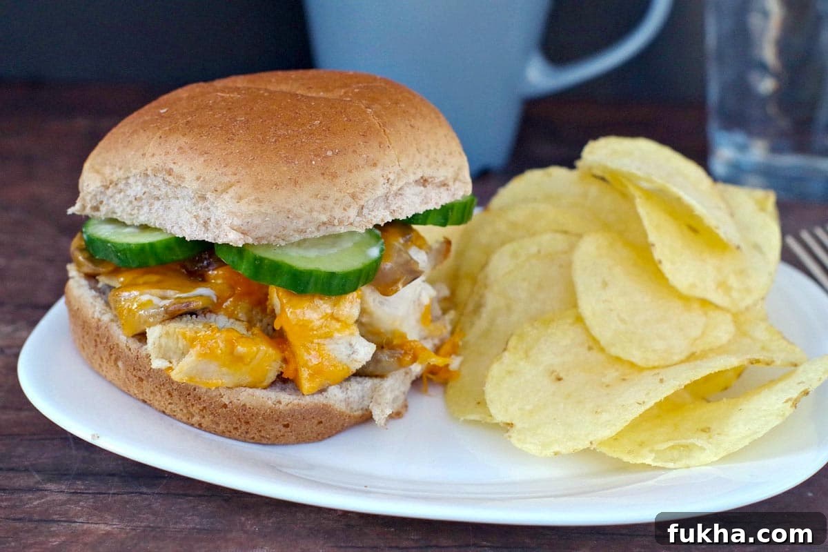 Juicy Grilled Chicken Breast Burger Recipe 2 chicken breast burger on a white plate with potato chip and blue coffee mug in the background