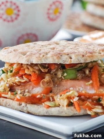 salmon burger on white plate with coleslaw, buns on a plate and sriracha mayo in background