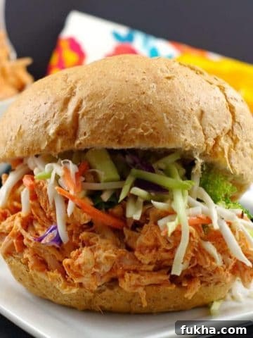 rotisserie chicken sandwich on a white plate with shredded chicken in background
