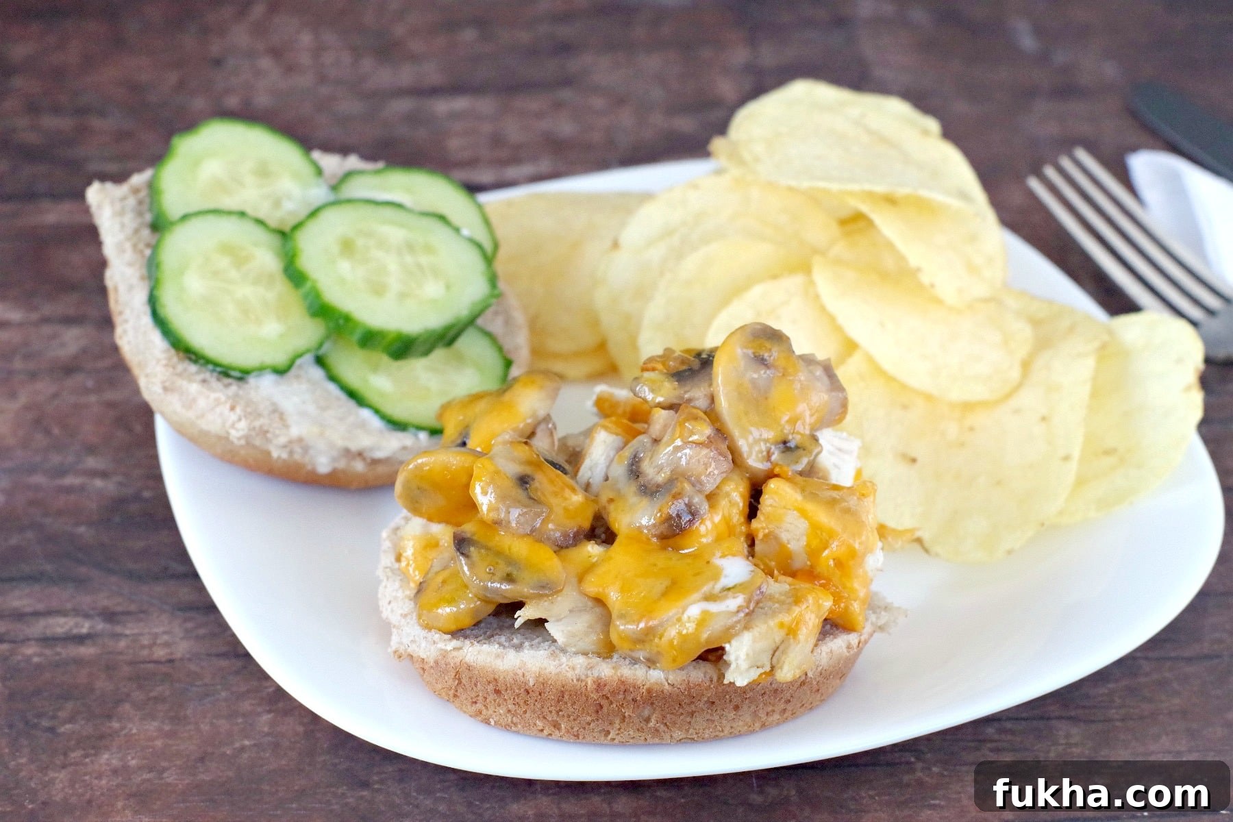 Juicy Grilled Chicken Breast Burger Recipe 8 chicken breast sandwich on plate with chicken and mushrooms on one side and cucumber on other side of bun